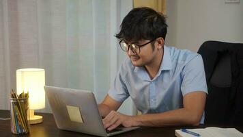 Aziatisch Mens glimlachen werken online met laptop Bij huis kantoor, telewerken concept. foto