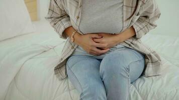 Aziatisch jong vrouw lijden van buik pijn terwijl zittend in bed Bij huis. foto