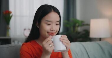 Aziatisch vrouw drinken een koffie terwijl zittend Aan de sofa foto