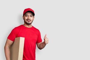 bezorger werknemer in rode dop leeg t-shirt vinger uniform houd lege kartonnen doos geïsoleerd op een witte achtergrond foto