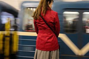 een mooie vrouw in een rood jasje die wacht op de komst van een trein in het metrostation foto