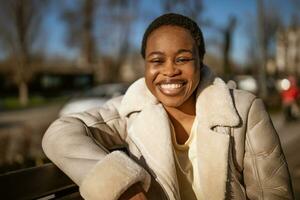 buitenshuis dichtbij omhoog portret van gelukkig Afro-Amerikaans vrouw Aan zonnig dag. foto