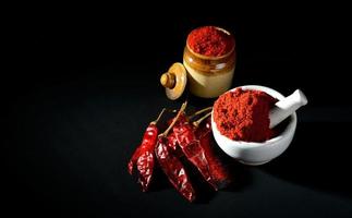 rode chili peper poeder in stamper met vijzel en aarden pot met rode chili pepers op zwarte achtergrond