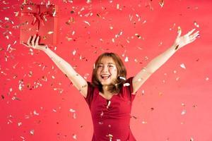 Aziatisch jong meisje in jurk met rode geschenkdoos met vrolijke uitdrukking op achtergrond