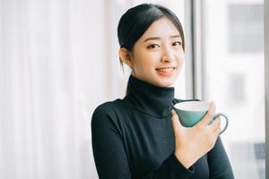 Aziatische vrouw die tijdens de pauze koffie drinkt bij het raam foto