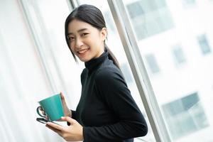 Aziatische vrouw die tijdens de pauze koffie drinkt bij het raam foto