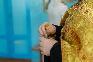 de handen van een orthodox priester houden een fles van mirre olie voor de rite van doop. foto