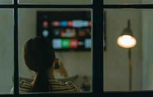 wazig beeld van een aziatische vrouw die 's nachts alleen televisie op de bank zit te kijken foto