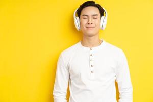 foto van een aziatische man in een wit overhemd die naar muziek luistert met zijn ogen dicht op een gele achtergrond