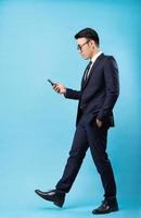 Aziatische zakenman die een pak draagt en op een blauwe achtergrond loopt