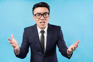 Aziatische zakenman die een pak draagt, voelt zich boos op een blauwe achtergrond foto