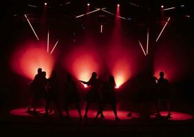 donker silhouetten van dansen meisjes tegen de achtergrond van rood licht van stadium schijnwerpers. foto