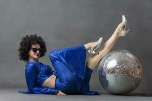 spectaculair vrouw in een sparkly uitlopend pak en afro pruik poses met een disco bal. disco stijl van de jaren zeventig of jaren tachtig. foto