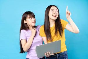 twee mooie jonge Aziatische meisjes met behulp van laptop op blauwe achtergrond