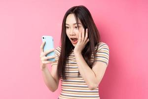 jonge aziatische vrouw die smartphone op roze achtergrond gebruikt foto