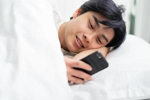aziatische man die in bed ligt en de telefoon gebruikt