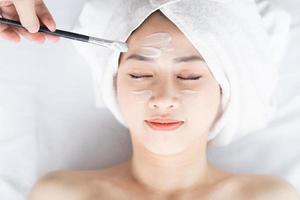 Aziatische vrouw doet schoonheidsbehandelingen, spabehandelingen en wordt crème op haar gezicht aangebracht foto