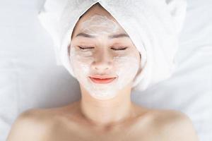Aziatische vrouw doet schoonheidsbehandelingen, spabehandelingen en wordt crème op haar gezicht aangebracht foto