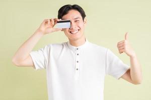 de knappe Aziatische zakenman lacht en bedekt zijn ogen met zijn creditcard terwijl zijn duimen omhoog