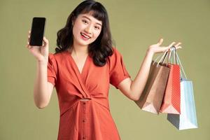 Aziatische vrouw die boodschappentas vasthoudt en telefoon omhoog houdt met leeg scherm blank foto