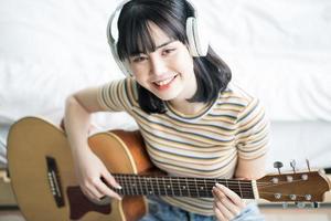 jong Aziatisch meisje oefent gitaar thuis en componeert muziek foto