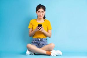 jonge aziatische vrouw zit en gebruikt smartphone op blauwe achtergrond foto