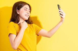 jonge Aziatische meisje uisng smartphone op gele achtergrond foto