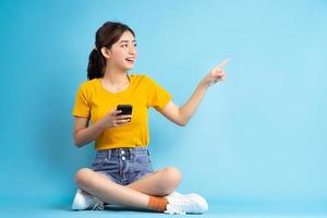 jonge aziatische vrouw zit en gebruikt smartphone op blauwe achtergrond foto