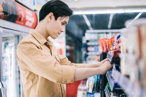 jonge Aziatische man vroeg zich af tijdens het winkelen in de supermarkt 's nachts foto