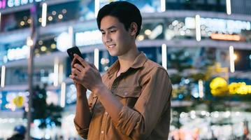 jonge aziatische man gebruikt zijn telefoon terwijl hij 's nachts op straat loopt foto