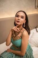 een Aziatisch vrouw met een goud ketting en oorbellen is poseren prachtig in een hotel kamer voordat avondeten foto