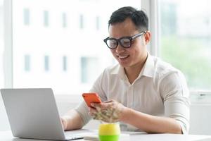jonge Aziatische zakenman die smartphone en laptop op kantoor gebruikt