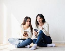 twee mooie vrouwelijke vrienden die berichten sturen met mobiele telefoons