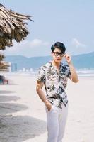 jonge aziatische man die op het strand loopt foto
