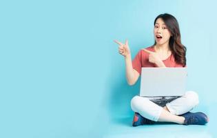 mooie aziatische vrouw die met laptop zit en zijwaarts wijst foto
