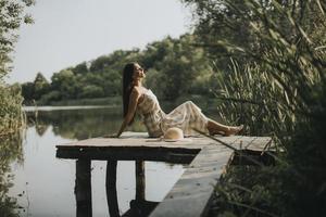 ontspannende jonge vrouw op houten pier aan het meer foto