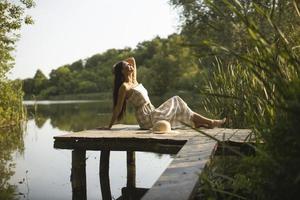 ontspannende jonge vrouw op houten pier aan het meer foto