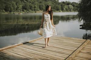 ontspannende jonge vrouw die op een houten pier aan het meer staat foto