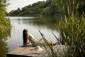 ontspannende jonge vrouw op houten pier aan het meer foto