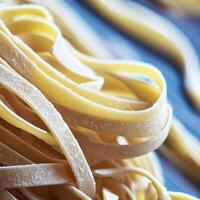 dichtbij omhoog van een rauw droog Italiaans pasta fettuccine Aan blauw houten tafel. ai generatief foto