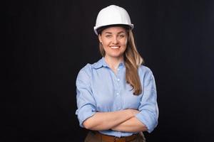 foto van een glimlachende jonge architectenvrouw die een witte helm draagt over een donkere achtergrond