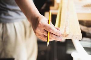 een timmerman meet de planken om de onderdelen te monteren en een houten tafel voor de klant te bouwen. foto
