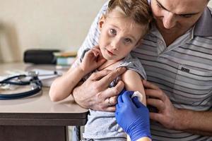 een klein meisje met haar vader in de spreekkamer van de kliniek wordt ingeënt tegen het coronavirus. het concept van vaccinatie, immunisatie, preventie tegen covid-19. foto