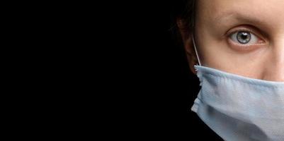 banner van het gezicht van een vrouw met een medisch masker op zwarte achtergrond, een uitbraak van coronavirusinfectie en bescherming ertegen. close-up, studioportret op donker. kopieer ruimte, kijk naar de camera foto