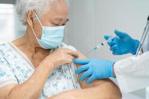 oudere aziatische senior vrouw met gezichtsmasker die covid-19 of coronavirusvaccin krijgt door een arts, maakt injectie. foto