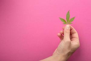 vrouwelijke hand met cannabisblad op roze achtergrond kopie ruimte, marihuana huidverzorging