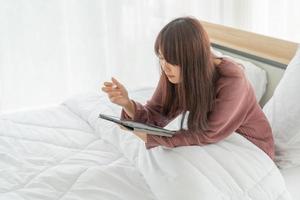 mooie aziatische vrouw die met tablet op bed werkt