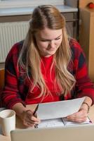 lachende blonde vrouw zit op een laptop thee drinken en werken. foto