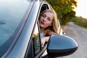 een jonge, mooie vrouw met lang haar zit aan het stuur van de auto en kijkt uit het raam. foto