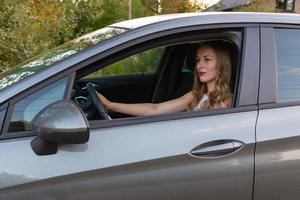 een jonge, mooie vrouw met lang haar zit aan het stuur van de auto. foto